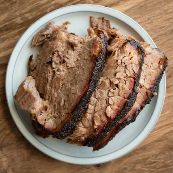 Sliced smoked brisket with bark on a white plate