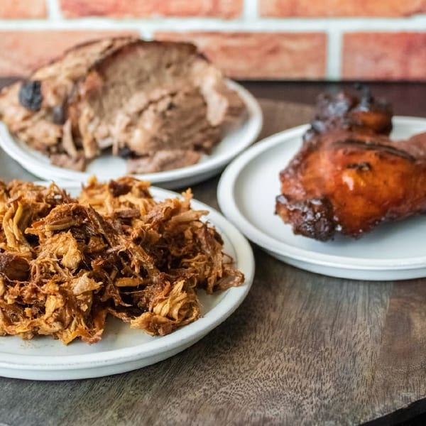 Pulled pork, sliced brisket, and a glazed BBQ chicken leg on white plates